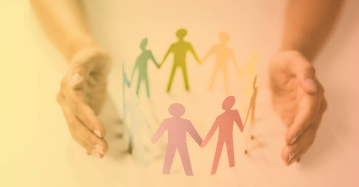 A visual metaphor of support and unity: two hands gently hold diverse cutouts of human figures. This image resonates with the discussion in the blog about the 12 benefits of emotional intelligence training for leaders and managers, emphasising the value of fostering an inclusive workplace culture.